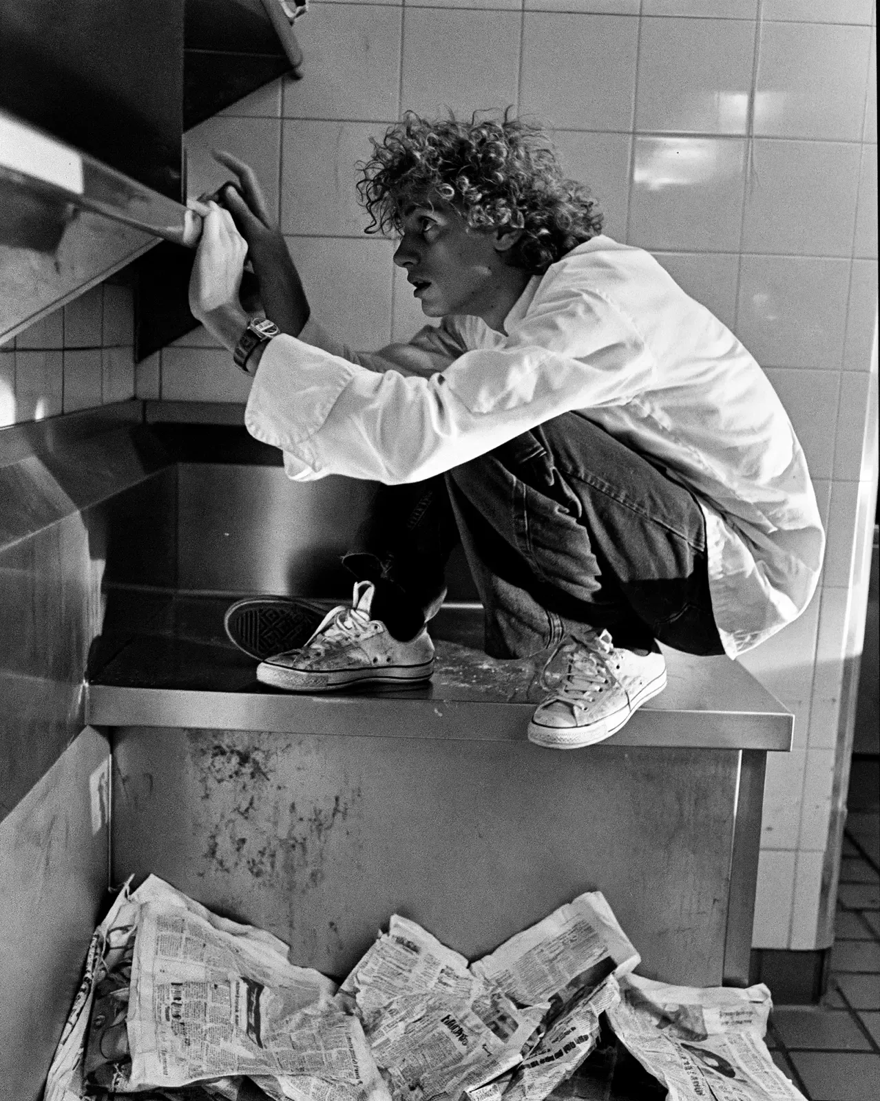 Jeune chef concentré dans une cuisine carrelée, en noir et blanc