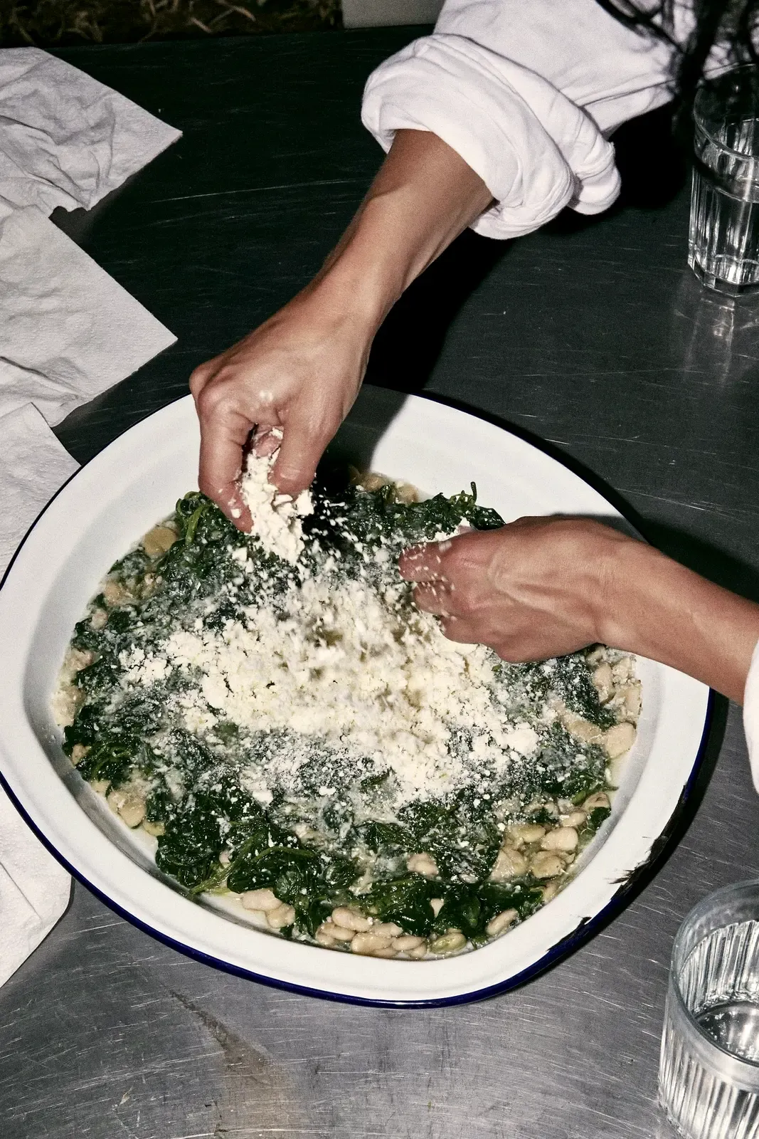 Deux mains qui émiettent de la feta sur un plat, en cuisine