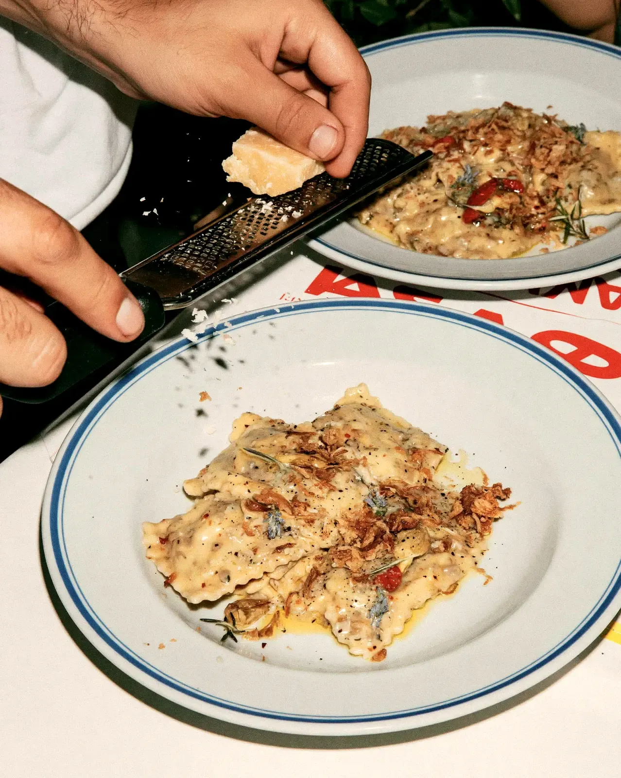 Mains qui râpent du parmesan sur deux assiettes de ravioles
