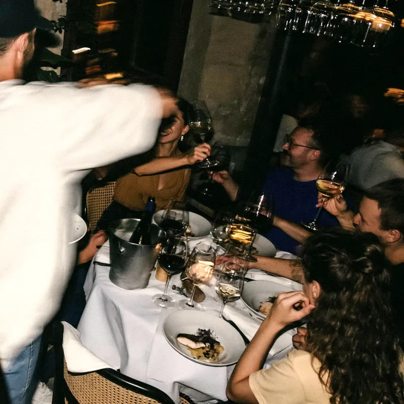 Salle de restaurant pleine un soir de service, des convives trinquent autour d'une table